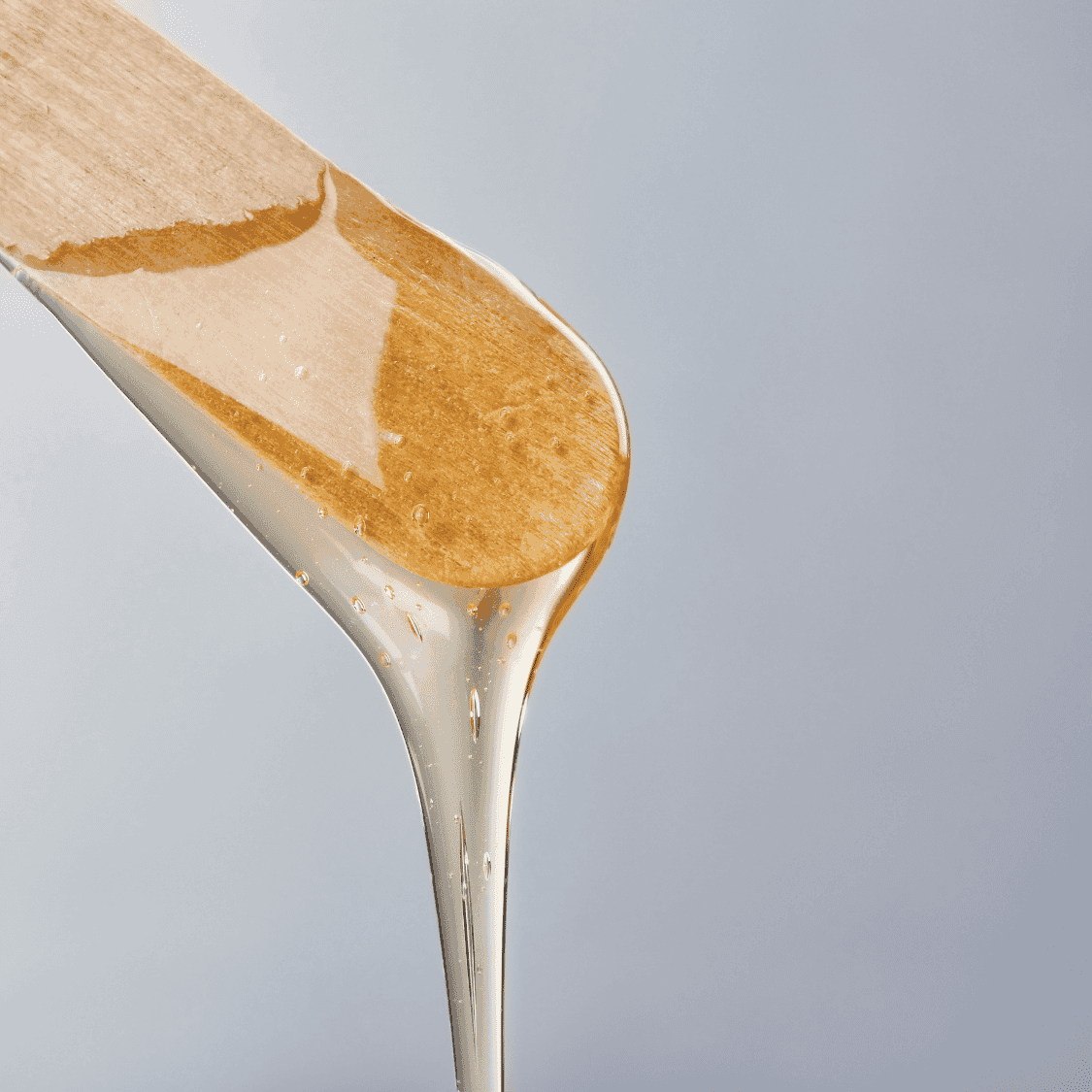 Wooden spatula with honey dripping against a light gray background.