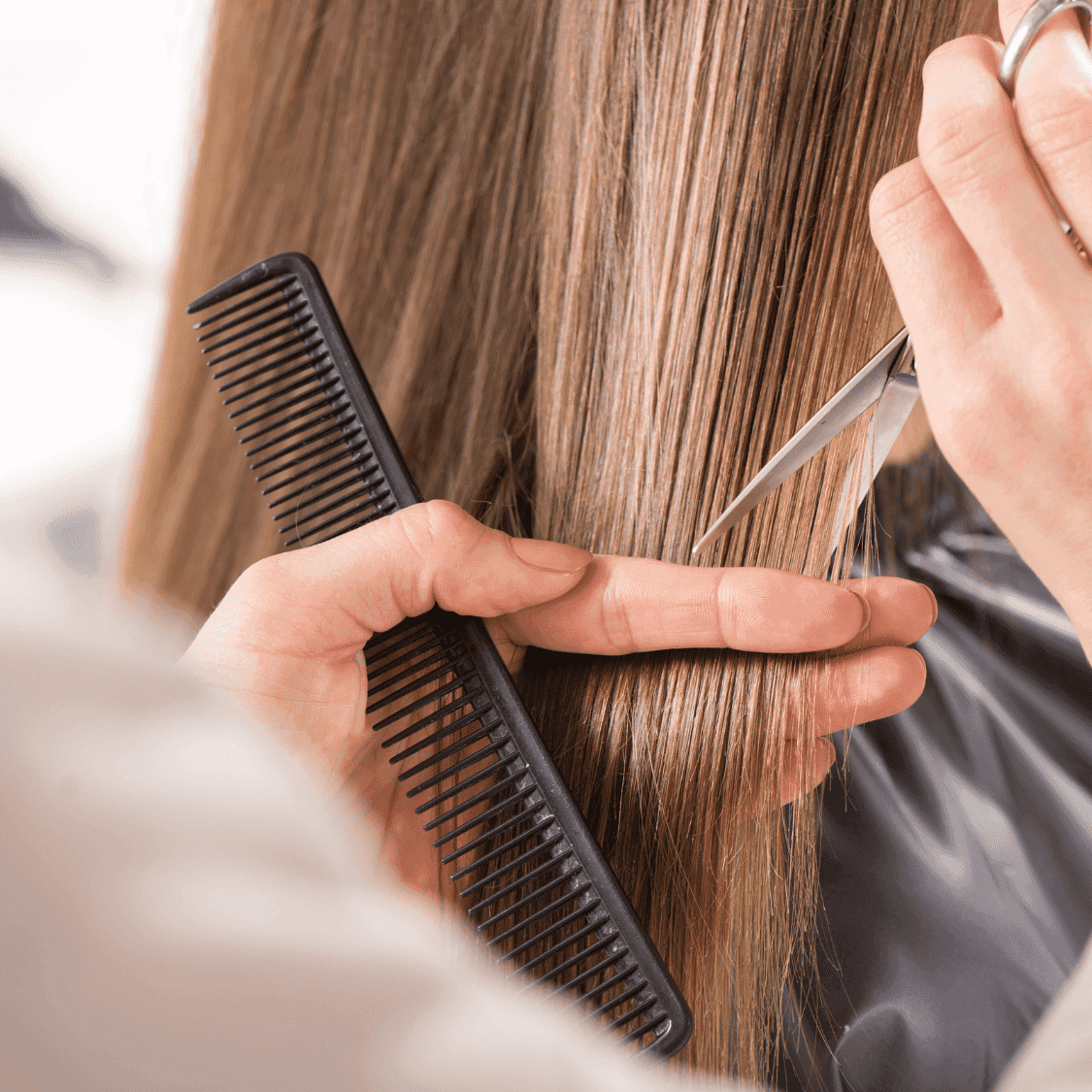 A stylist cuts straight brown hair with scissors and comb for a precise haircut.